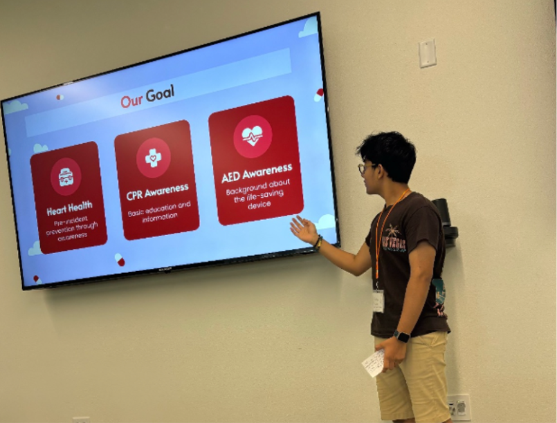 An HFH volunteer presents a slide titled Our Goal, covering heart health, CPR awareness, and AED awareness